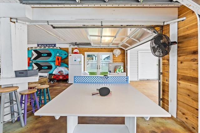 game room featuring wooden walls, concrete floors, and a garage