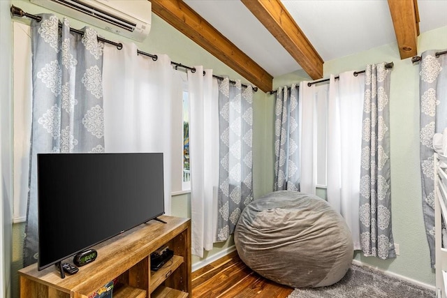 bedroom with a wall mounted air conditioner, beam ceiling, and wood finished floors