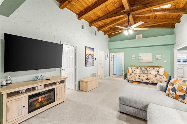 living room with ceiling fan, light carpet, a glass covered fireplace, wooden ceiling, and beamed ceiling