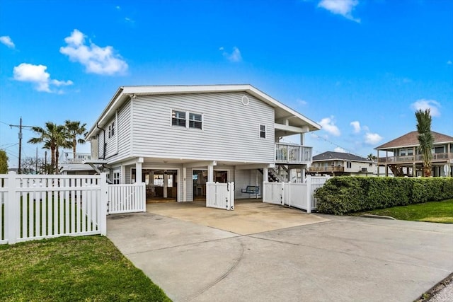 raised beach house featuring a balcony, a gate, fence, a carport, and concrete driveway