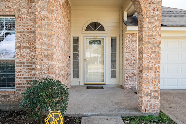 doorway to property featuring a garage, brick siding, and roof with shingles