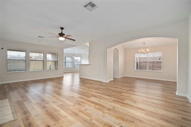 unfurnished living room featuring visible vents, ceiling fan with notable chandelier, arched walkways, light wood finished floors, and baseboards