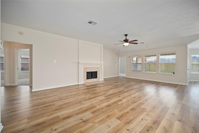 unfurnished living room featuring light wood finished floors, visible vents, baseboards, ceiling fan, and a tile fireplace