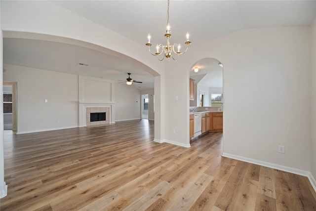 unfurnished living room featuring light wood finished floors, baseboards, a tiled fireplace, lofted ceiling, and arched walkways