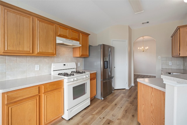 kitchen with visible vents, white gas stove, under cabinet range hood, arched walkways, and stainless steel fridge