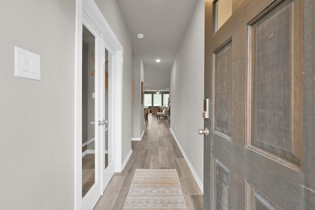 corridor featuring french doors, baseboards, and light wood-style flooring