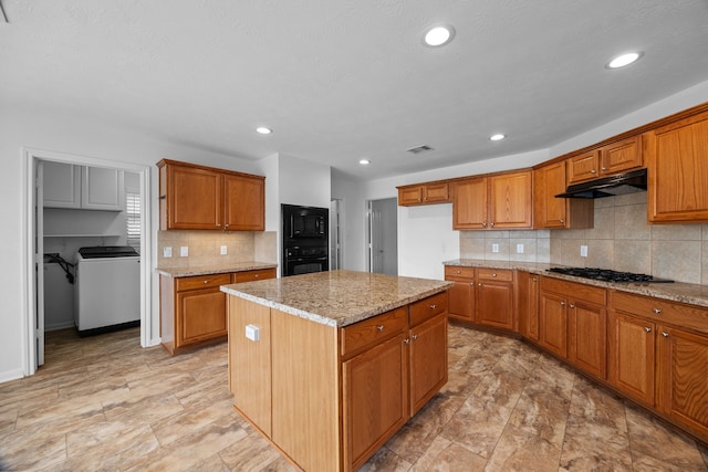 kitchen featuring under cabinet range hood, black appliances, brown cabinetry, and light stone countertops