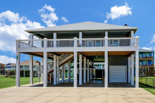 rear view of property with concrete driveway, stairs, roof with shingles, a lawn, and a carport