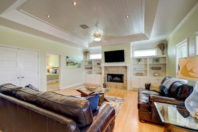 living room featuring light wood-style flooring, a fireplace, a raised ceiling, and ornamental molding