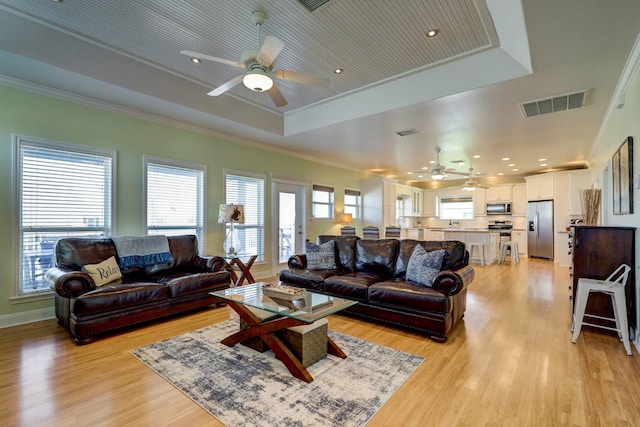 living room featuring a tray ceiling, crown molding, visible vents, and light wood finished floors