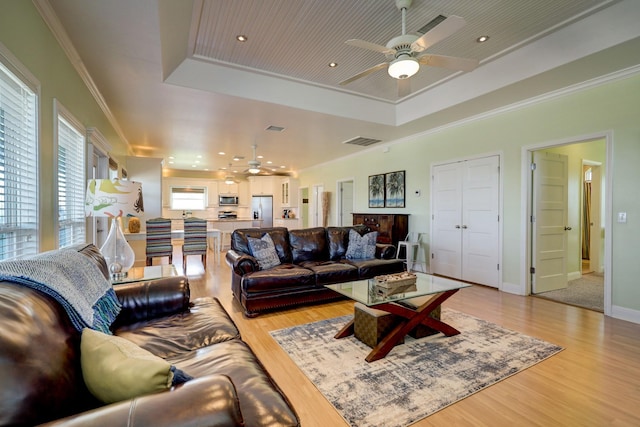 living area featuring a tray ceiling, light wood-style flooring, crown molding, and visible vents