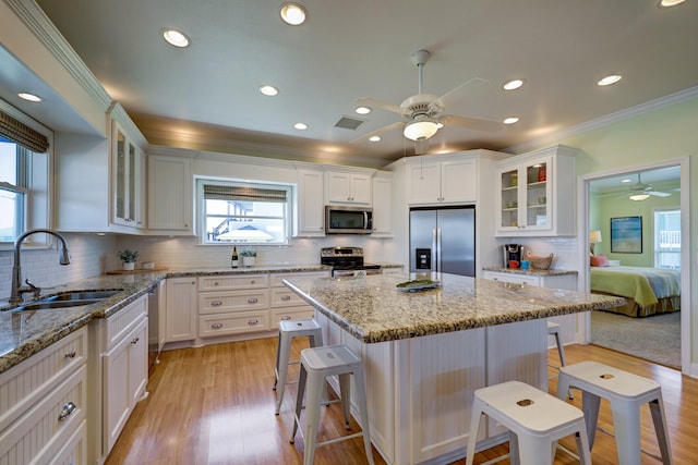 kitchen with a kitchen bar, ornamental molding, a sink, white cabinetry, and appliances with stainless steel finishes