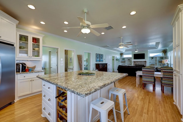 kitchen featuring visible vents, a kitchen breakfast bar, stainless steel fridge, white cabinets, and a fireplace