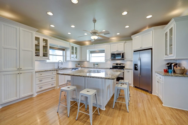 kitchen with a sink, white cabinetry, light wood-style floors, appliances with stainless steel finishes, and a breakfast bar area