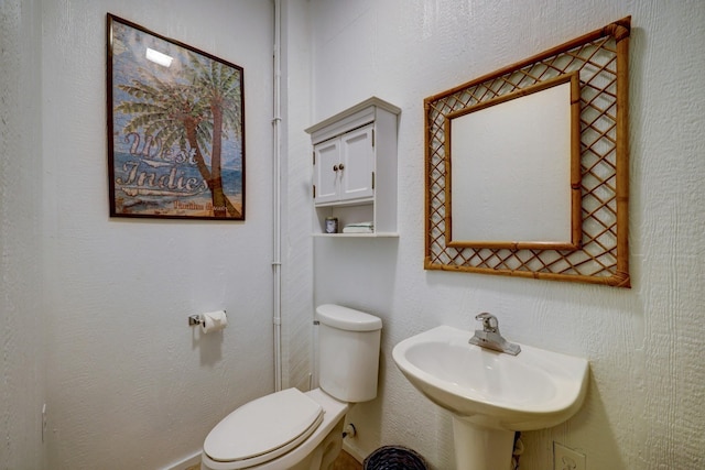 bathroom with toilet, a textured wall, and a sink