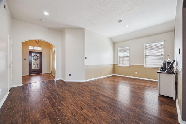 foyer entrance with visible vents, arched walkways, dark wood-type flooring, and vaulted ceiling