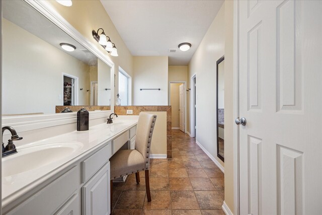 full bathroom with double vanity, baseboards, and a sink