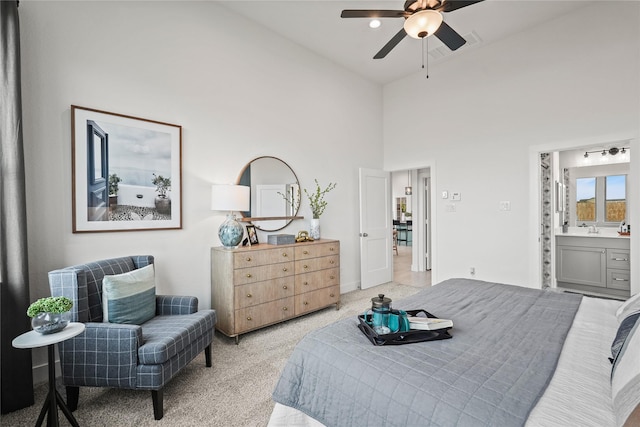 bedroom with a ceiling fan, ensuite bath, light colored carpet, and a towering ceiling