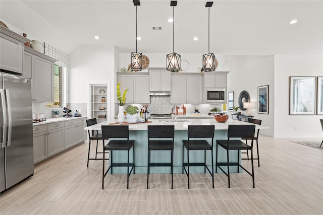 kitchen featuring gray cabinetry, built in microwave, a breakfast bar, light countertops, and freestanding refrigerator