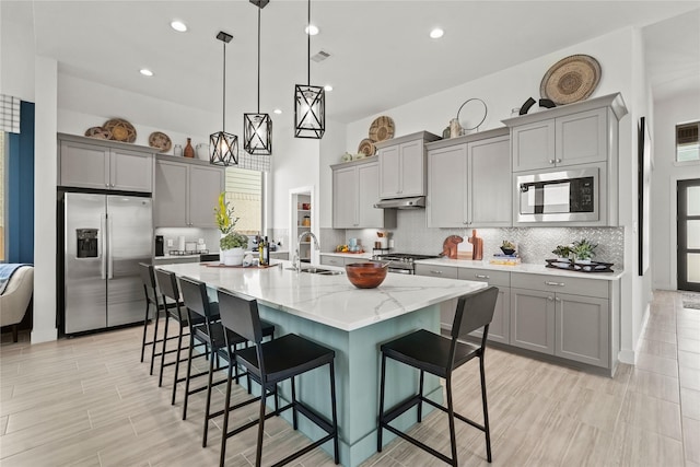 kitchen featuring visible vents, gray cabinetry, under cabinet range hood, appliances with stainless steel finishes, and a sink