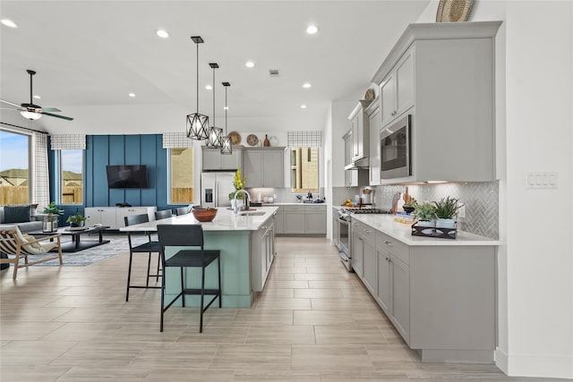 kitchen with gray cabinetry, open floor plan, light countertops, stainless steel appliances, and a sink