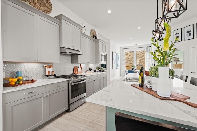 kitchen featuring gray cabinets, a sink, stainless steel appliances, under cabinet range hood, and backsplash