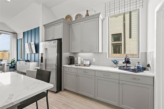 kitchen featuring vaulted ceiling, decorative backsplash, gray cabinetry, and stainless steel fridge with ice dispenser