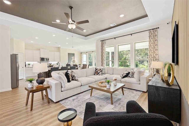 living room with recessed lighting, a tray ceiling, visible vents, and light wood finished floors