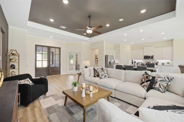 living area featuring a tray ceiling, french doors, light wood-type flooring, and ornamental molding