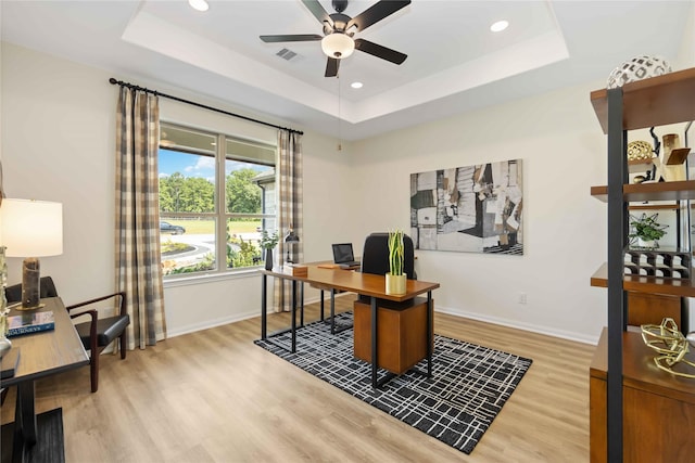 office area with a raised ceiling, light wood-style floors, visible vents, and baseboards