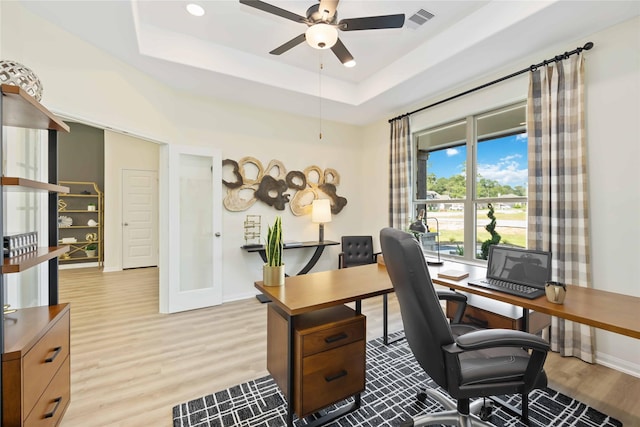 office featuring baseboards, visible vents, ceiling fan, a raised ceiling, and light wood-type flooring