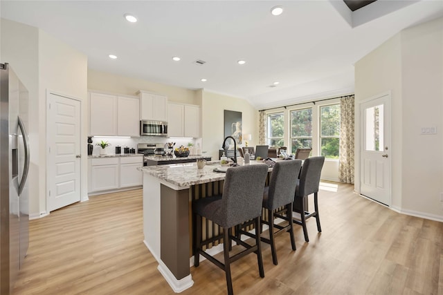 kitchen featuring a breakfast bar area, light wood finished floors, white cabinets, and appliances with stainless steel finishes