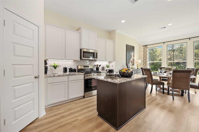 kitchen with a kitchen island, backsplash, stainless steel appliances, and light stone countertops