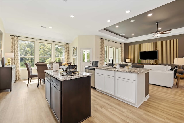 kitchen with a sink, light stone countertops, dishwasher, and an island with sink