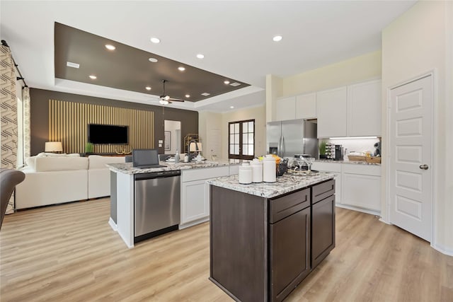 kitchen with open floor plan, a tray ceiling, appliances with stainless steel finishes, white cabinets, and a kitchen island with sink