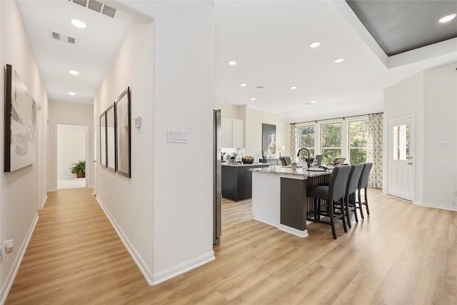 kitchen featuring visible vents, a center island with sink, a breakfast bar area, and light wood-style flooring