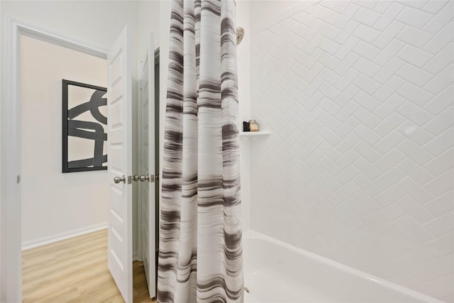 room details featuring wood finished floors, baseboards, and shower / bathtub combination with curtain