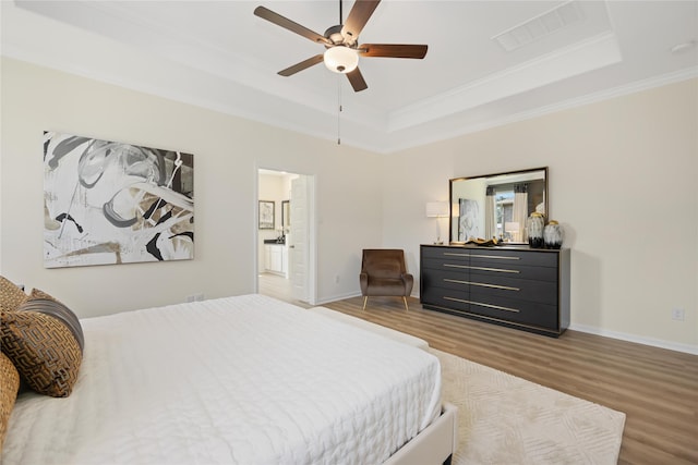 bedroom with visible vents, crown molding, baseboards, a tray ceiling, and wood finished floors