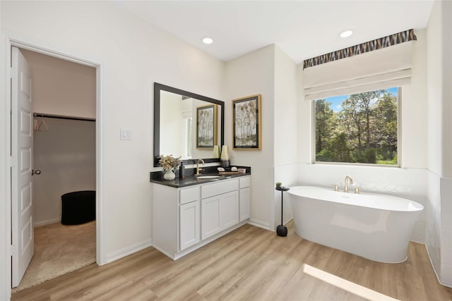 full bath featuring vanity, a freestanding bath, a walk in closet, and wood finished floors