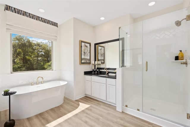 bathroom featuring wood finished floors, recessed lighting, a shower stall, a freestanding bath, and vanity