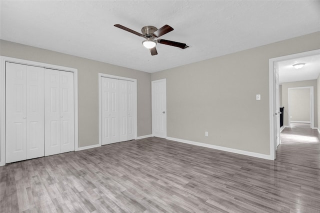 unfurnished bedroom with ceiling fan, two closets, baseboards, and wood finished floors