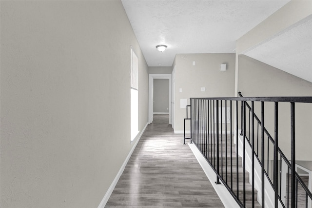 hall featuring an upstairs landing, lofted ceiling, a textured ceiling, wood finished floors, and baseboards