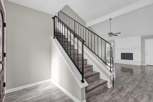 stairs featuring lofted ceiling with beams, baseboards, a brick fireplace, and wood finished floors