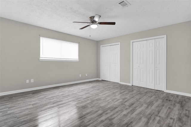 unfurnished bedroom featuring visible vents, baseboards, two closets, and wood finished floors