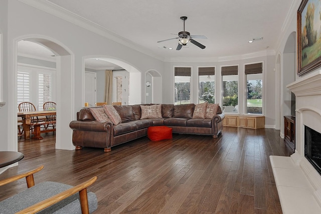 living area featuring crown molding, a healthy amount of sunlight, dark wood-style flooring, and a fireplace with raised hearth