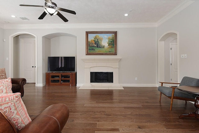 living area with wood finished floors, a fireplace with raised hearth, visible vents, and ornamental molding