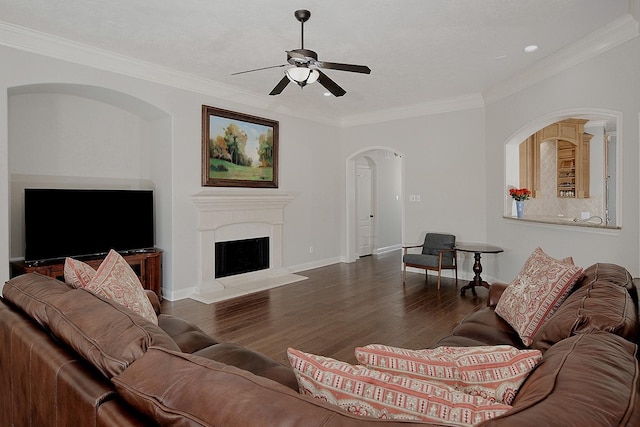 living room featuring wood finished floors, baseboards, a fireplace with raised hearth, ceiling fan, and crown molding