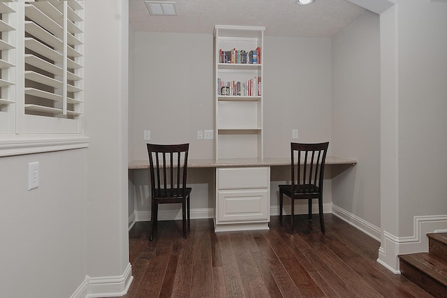 office space featuring a textured ceiling, built in study area, dark wood-type flooring, and baseboards