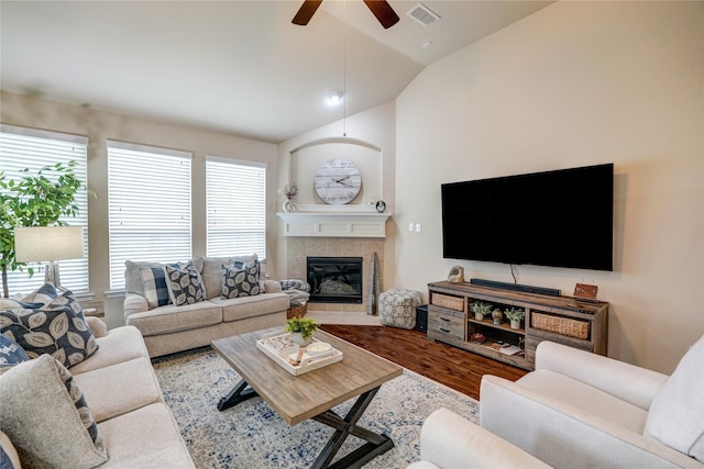 living room featuring visible vents, a ceiling fan, a tiled fireplace, wood finished floors, and vaulted ceiling