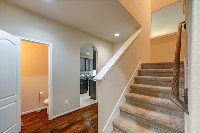 stairs with recessed lighting, wood finished floors, arched walkways, and baseboards